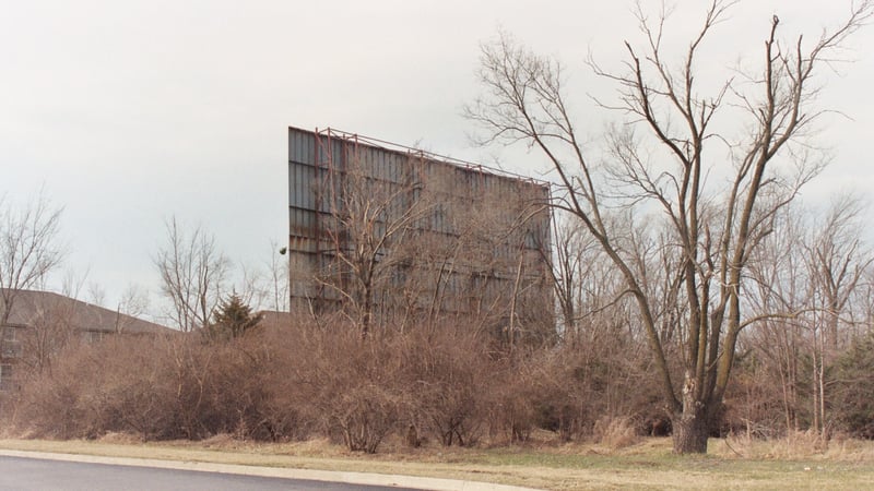 Two pictures of screentower surounded by overgrown brush. Screen has peeling paint and faces an apartment complex.