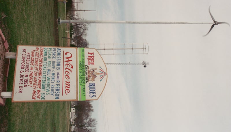 Sign describing particulars of theatre. Children's Carousel operates prior to movie showing when weather permits. Electricity to operate Carousel comes in part from wind generators.