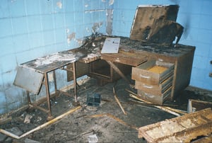 Dreary, windowless office with rusted desks.  Room is pitch black without the camera flash.