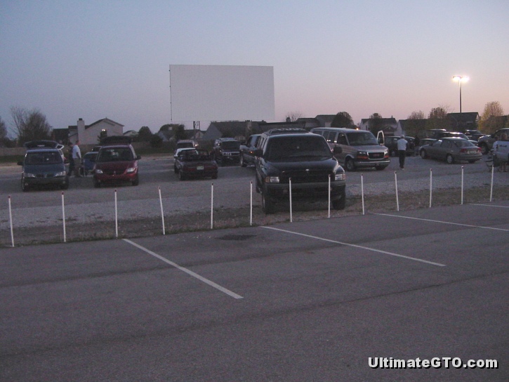 Cars are gathering in the gravel lot on a Saturday night in April.