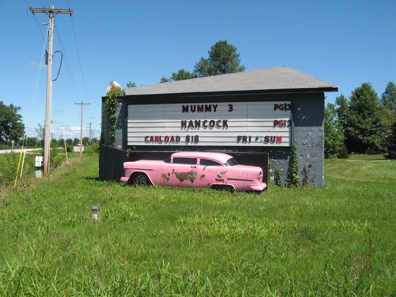 MARQUEE. ON THE OTHER SIDE IS THE OTHER HALF OF THE CAR. FLOODLIT AT NIGHT.