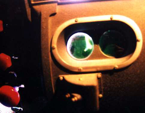 A view of the burning carbon arc, through the (smoked-glass) lamphouse viewing porthole.  The red and black knobs at left are some of the carbon and reflector adjustment controls.