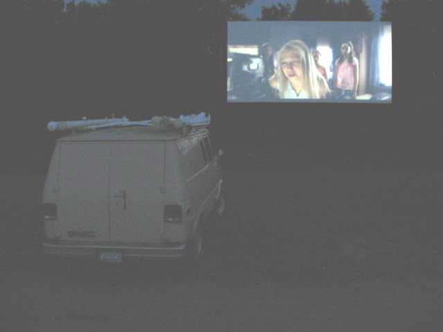 Screen playing movie with van in foreground.