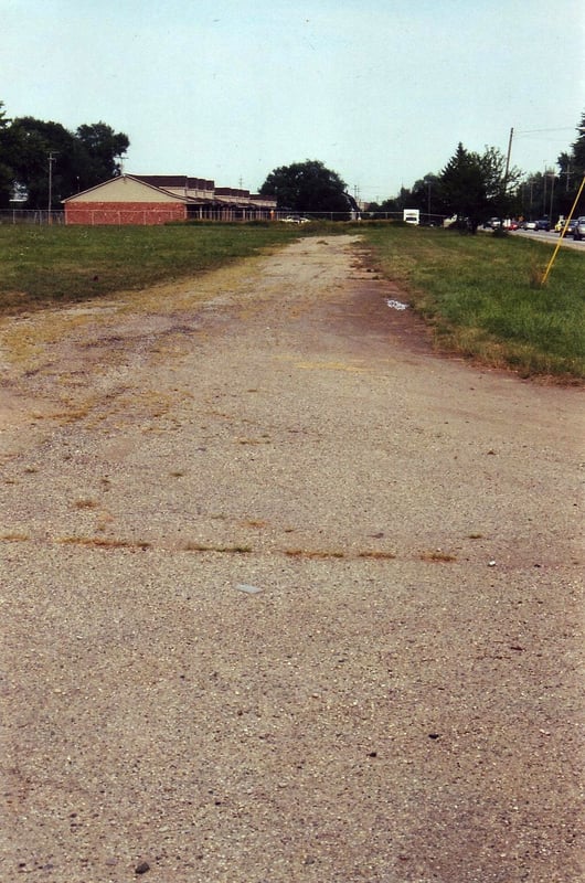 Former entrance road. The grass covered ticket booth slab is barely visible at the far end just below the tree