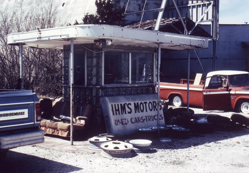 Ticket booth amidst wheel drums and junked cars. An old sofa sits also there