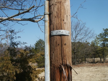 One of several unused remaining poles owned by Verizon (as indicated by the letters "BT" on pole tag - for Bell Telephone). Poles are along tree line on left side of field, near where speaker poles were found.