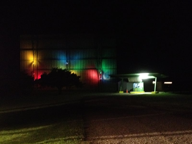 The back of screen 1 facing the road with colored lights on it and the box office at night.