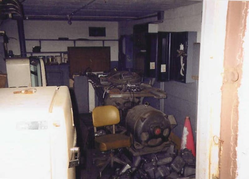 Storage room in back of projection building with lamphouses, speakers, fuse boxes, paint cans, refrigerators, hazard cone, and chair.