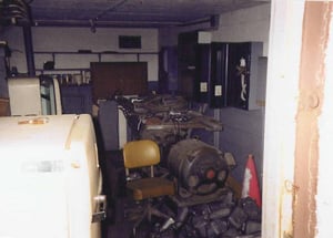 Storage room in back of projection building with lamphouses, speakers, fuse boxes, paint cans, refrigerators, hazard cone, and chair.