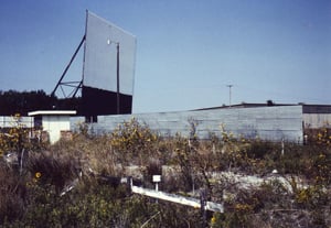 Very overgrown entrance road with ticket booth and the big screen