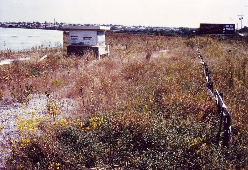 Entrance road overgrown with prairie grass and boarded up ticket booth