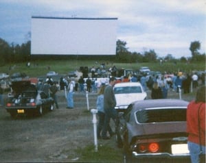 A view of Screen 1 Cinemascope towering over classic car enthusiasts at a car cruise sponsored by Pittsburgh's Country Y108