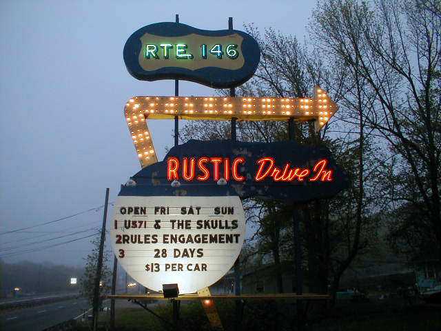 The vintage sign of the Rustic Tri-View Drive-In illuminating a misty spring evening