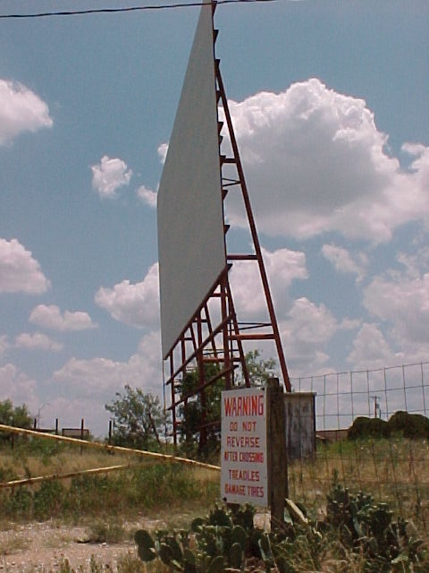 Screen still standing. Concession stand is gone and replaced with tan tin building. Ticket stand is still standing in poor condition.