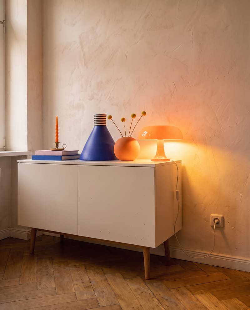 Sideboard Deko Idee im Dopamin Stil: orange Pilzlampe am Abend als einzige Lichtquelle neben Kegelvase, Kugelvase und Büchern