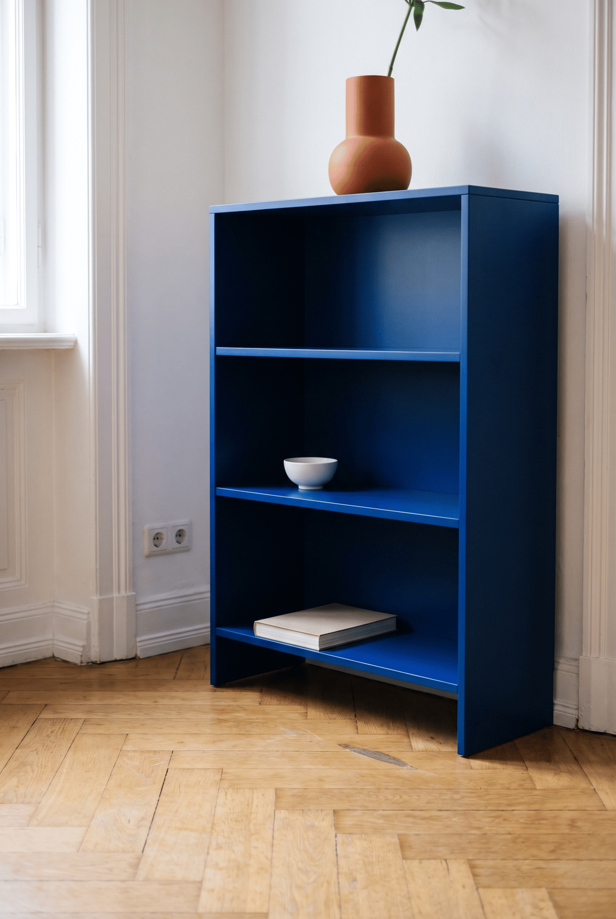 Regal Deko Idee im Dopamin Stil: kobaltblau lackiertes Regal mit orangefarbener Vase, weißer Schale und liegendem Buch im Altbau mit Fischgrätparkett