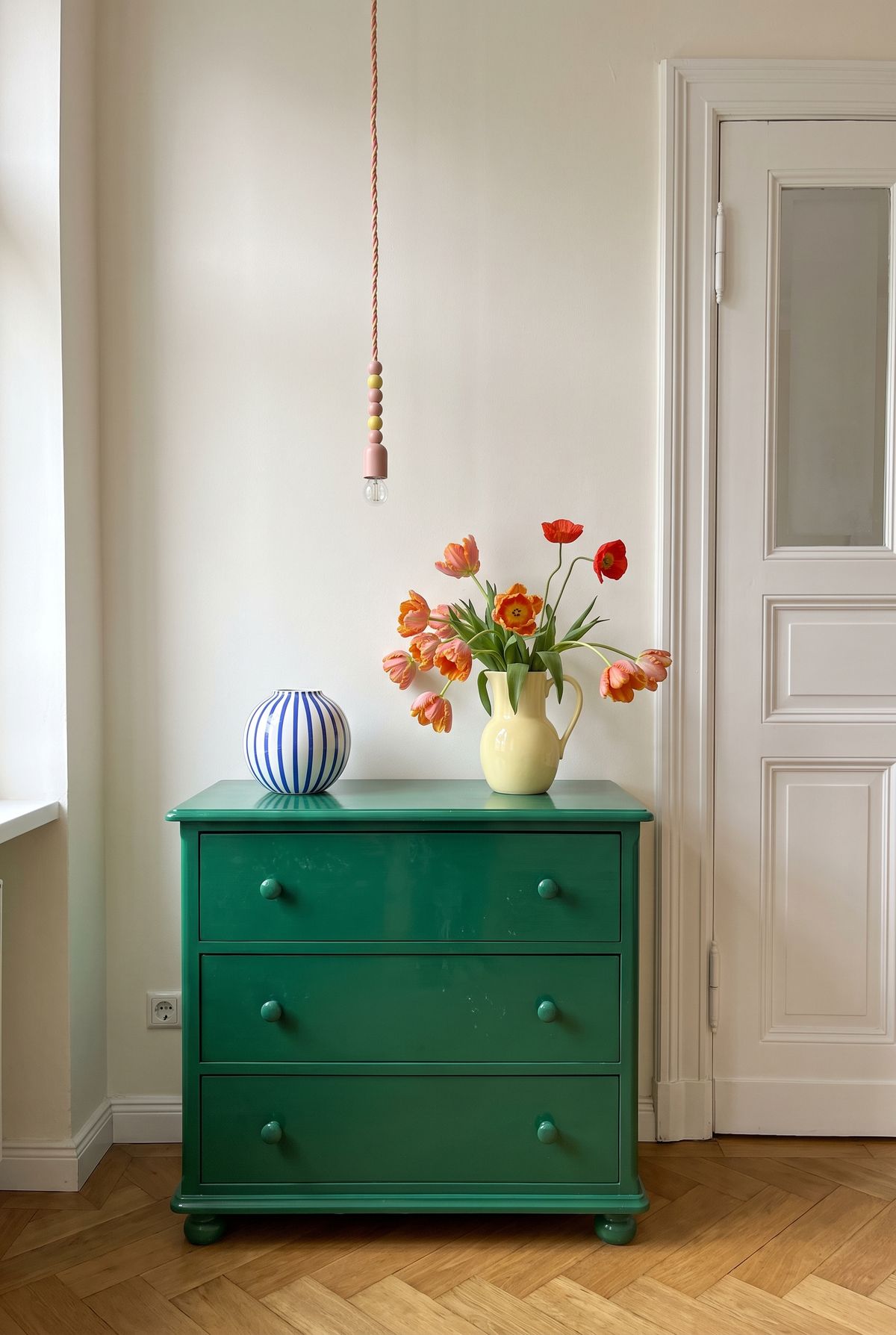 Sideboard Deko Idee im Dopamin Stil: blau-weiß gestreifte Kugelvase und gelber Krug mit Papageientulpen auf smaragdgrüner Kommode