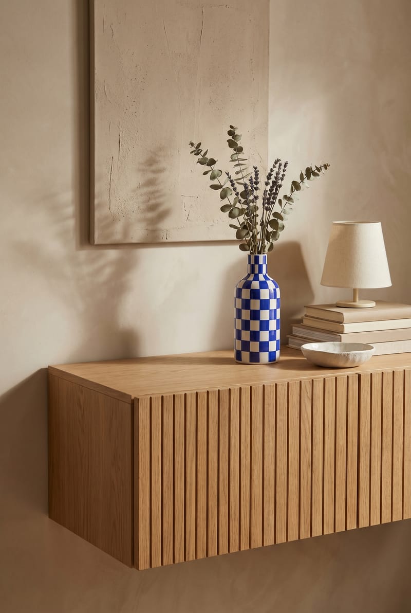 Sideboard-Styling mit blau-weißer Vase, Eukalyptus, Tischlampe und Büchern auf Lamellen-Sideboard