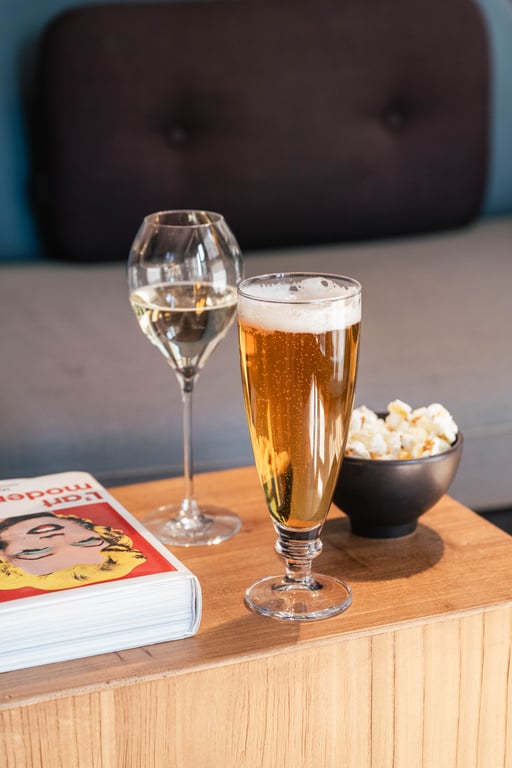 Verre de bière blonde et flûte de champagne sur table basse en bois avec du pop-corn et un magazine.