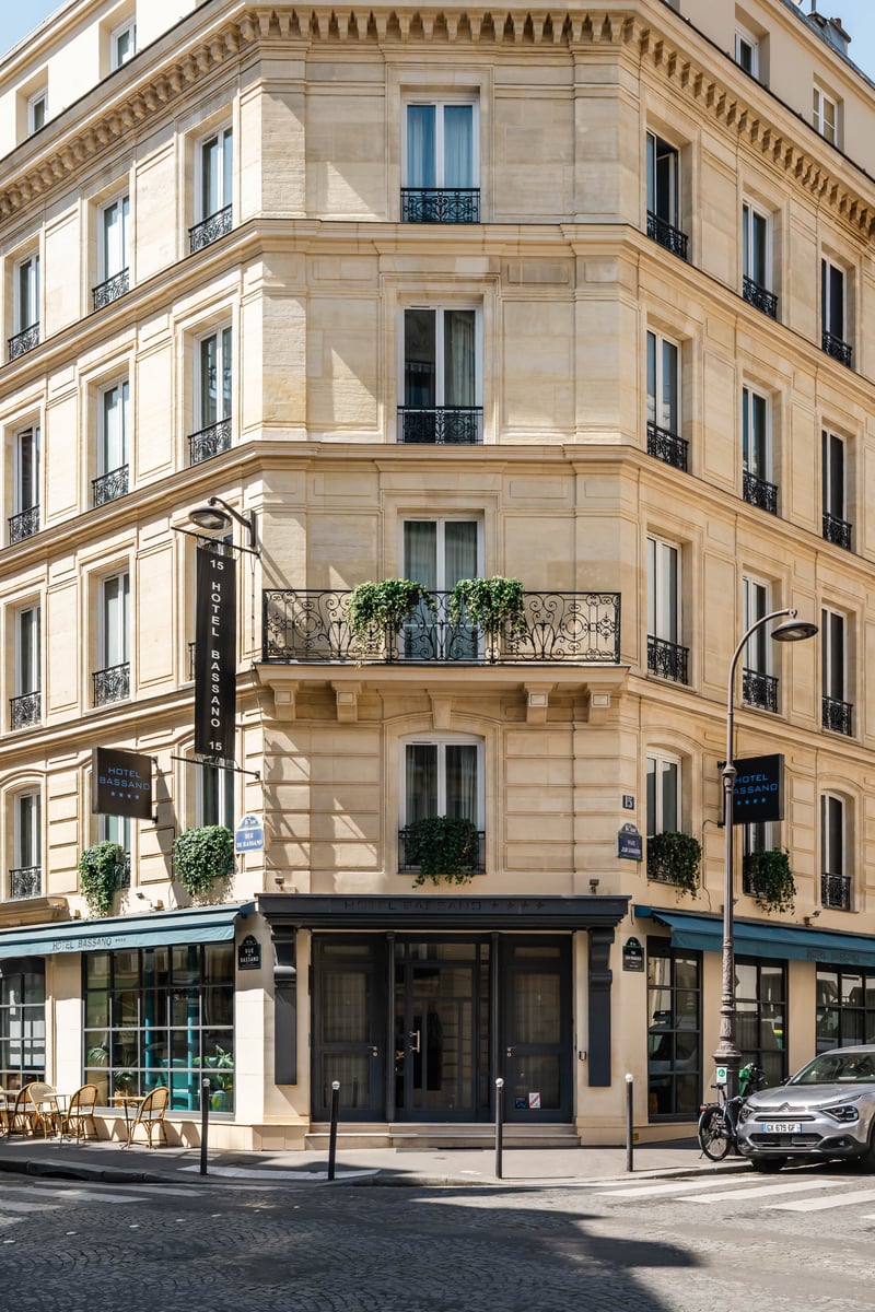 Façade d'hôtel haussmannien avec balcons fleuris, entrée au rez-de-chaussée et bandeaux signalétiques en façade.