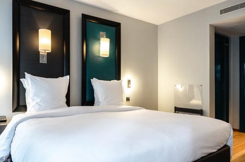 Chambre d'hôtel avec lit blanc, tête de lit noire avec appliques lumineuses et alcôves turquoise.