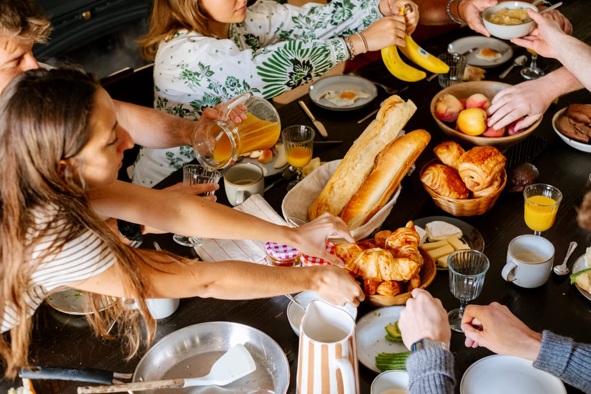 Petit-déjeuner convivial partagé autour d'une grande table : viennoiseries, baguettes, fruits et jus d'orange