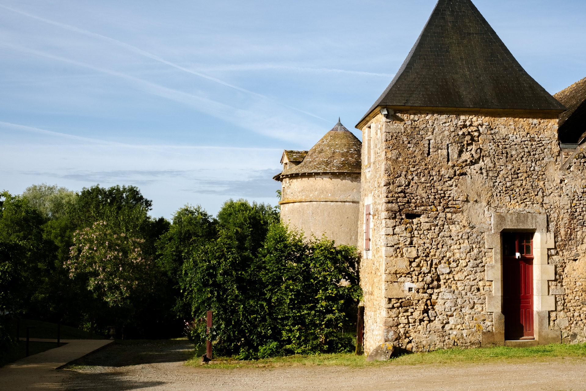 Bâtiments en pierre du Domaine de Fontenay : tour au toit d'ardoise conique et façade ancienne, sous un ciel bleu
