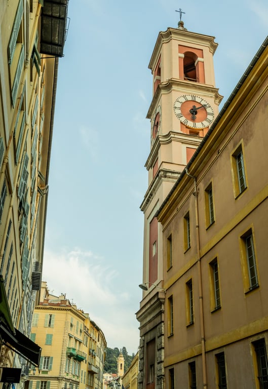 Clocher de l'église avec horloge dominant une rue historique bordée de bâtiments aux façades jaunes et ocre.