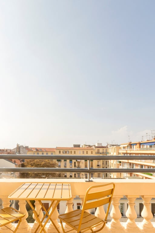 Terrasse d'hôtel avec chaise longue et table surplombant les toits ocre d'une ville côtière.