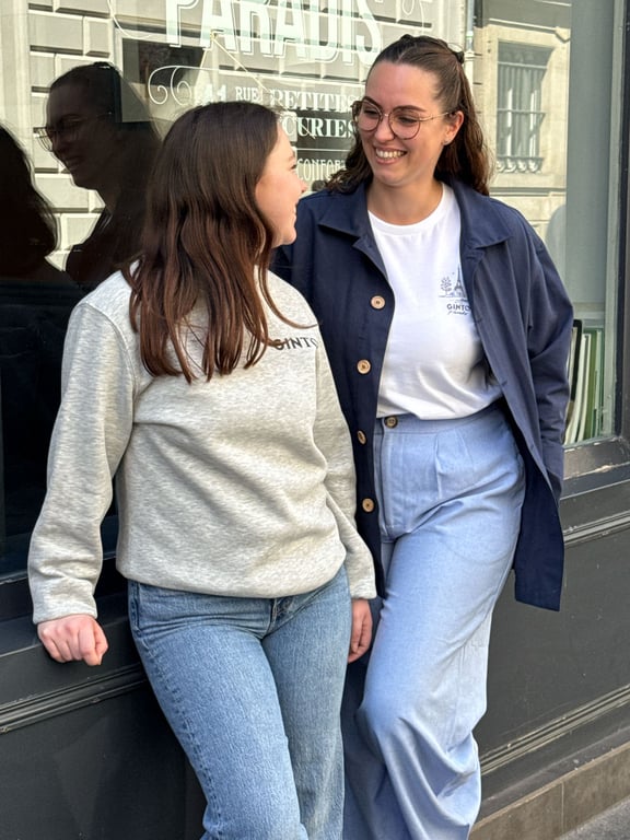 Two smiling young women chat in front of a Parisian shop window.