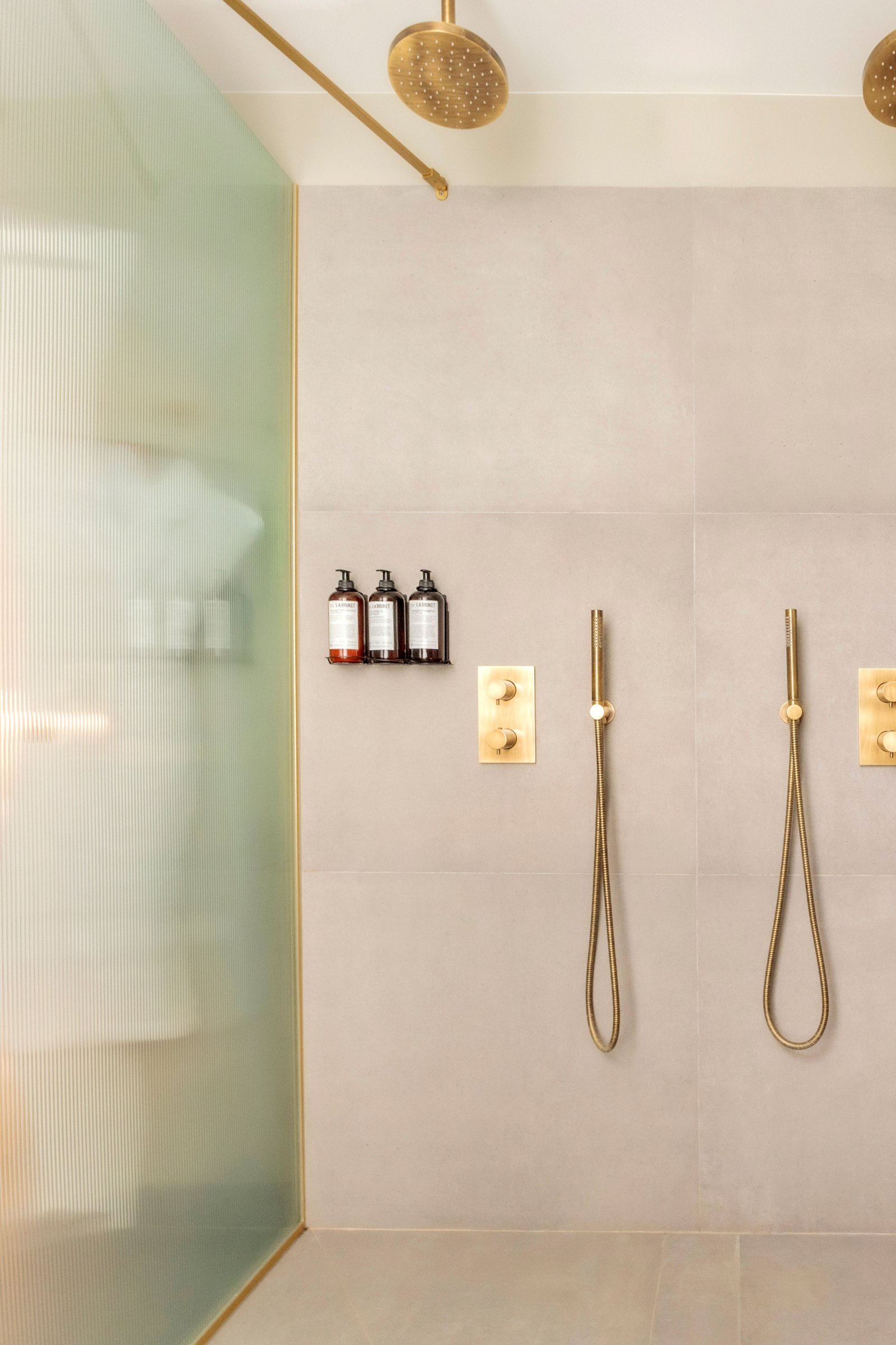 Douche contemporaine avec paroi verte texturée, robinetterie dorée, pommeau de douche rond et produits d'accueil.