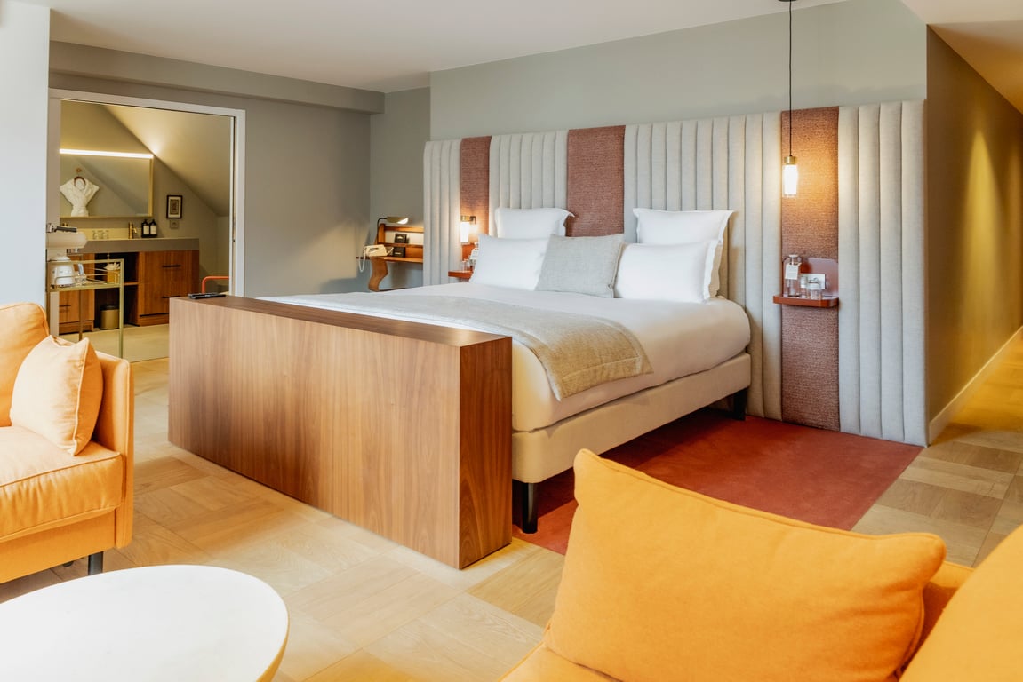 Chambre d'hôtel de luxe avec lit king-size, fauteuils jaunes, salle de bain attenante et éclairage ambiant chaleureux.