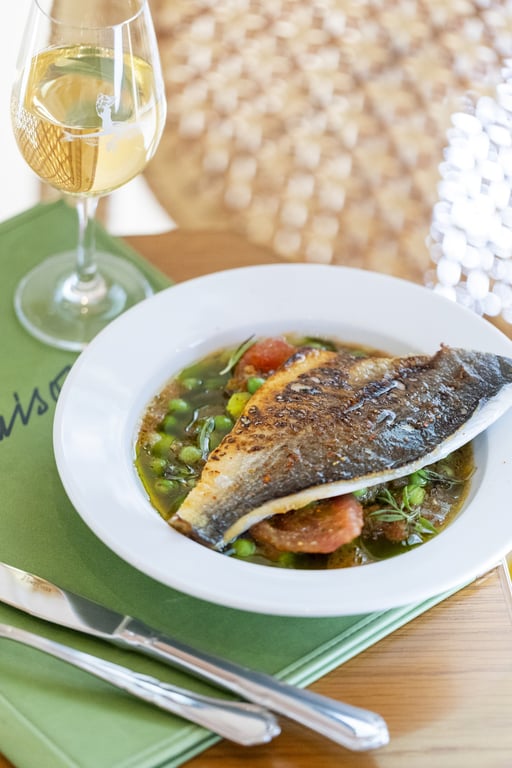 Un plat de la Table Louison à Amista : filet de poisson, petits pois et verre de vin blanc
