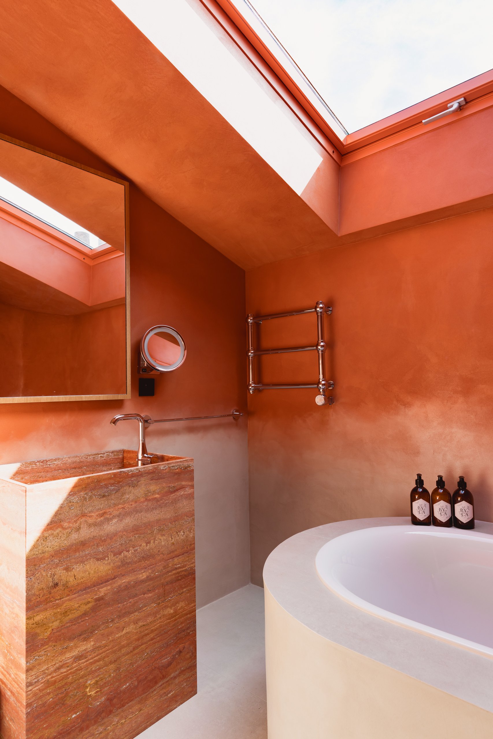 Salle de bain contemporaine avec murs orangés, baignoire ronde blanche, lavabo en pierre et puits de lumière zénithaux.