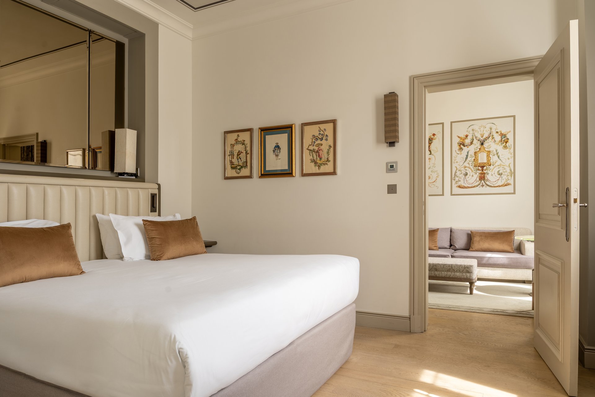 Suite élégante avec canapé gris, fauteuil beige, œuvres d'art florales et baies vitrées donnant sur la vue extérieure.