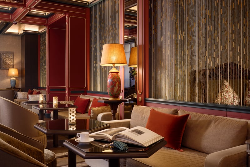 Salon luxueux avec panneaux rouges, lampes dorées, canapés beiges et mobilier élégant inspiré d'un design asiatique classique.