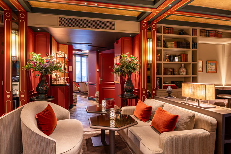 Salon d'une suite parisienne : canapé beige, miroir nacré et hautes fenêtres donnant sur la rue Frédéric Bastiat