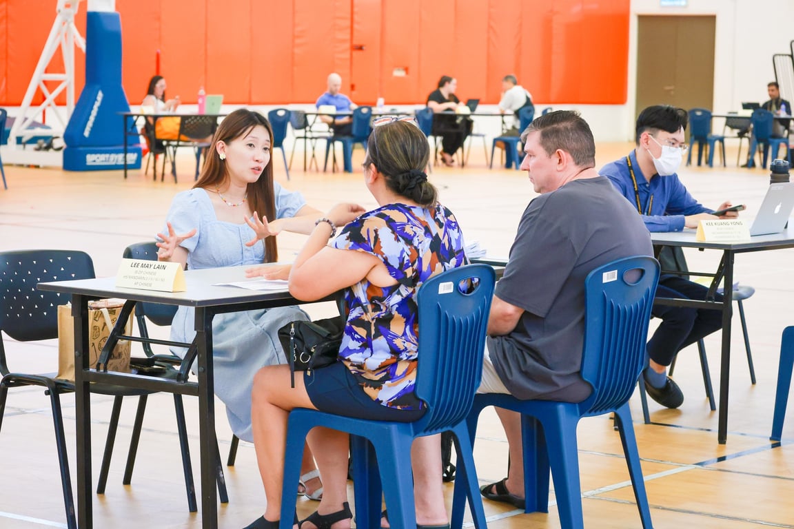 A teacher discussing student progress with parents during the Parent-Teacher Conference in the school gym.