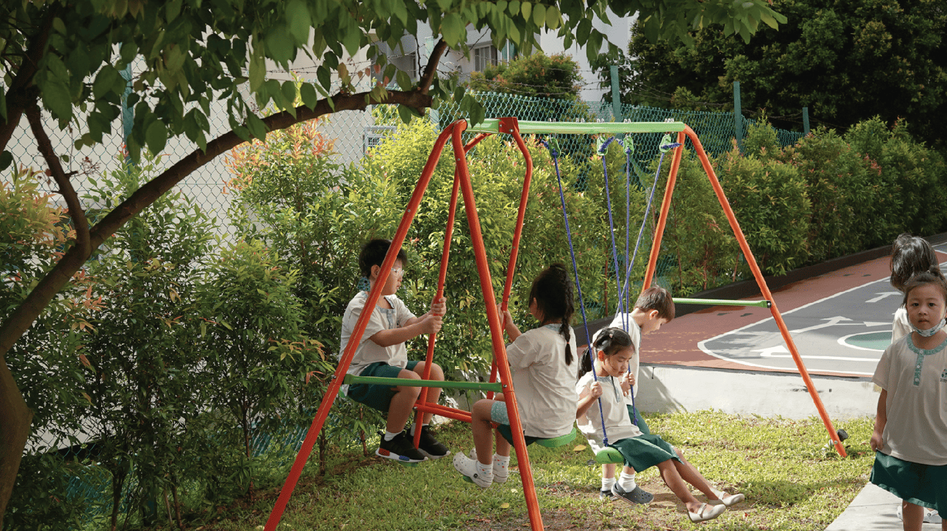 Children enjoy swinging outdoors under the shade of trees during playtime.