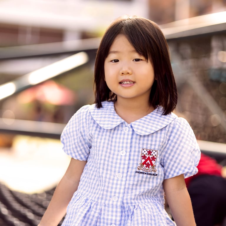 A young student in Early Years uniform smiles outdoors.