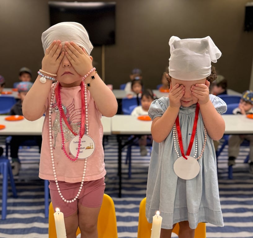 Nursery children covering their eyes during Shabbat candle lighting.
