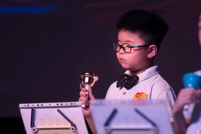 A young student concentrates during a handbell performance, showcasing musical discipline and focus.