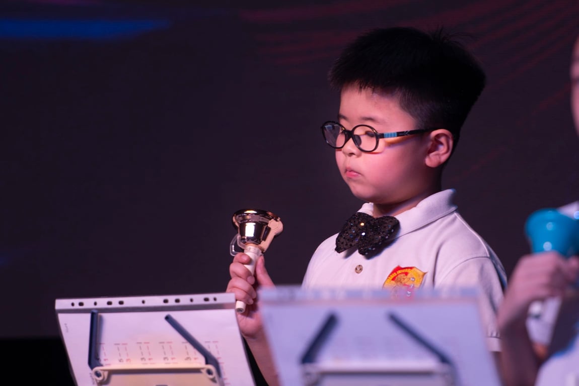 A young student concentrates during a handbell performance, showcasing musical discipline and focus.