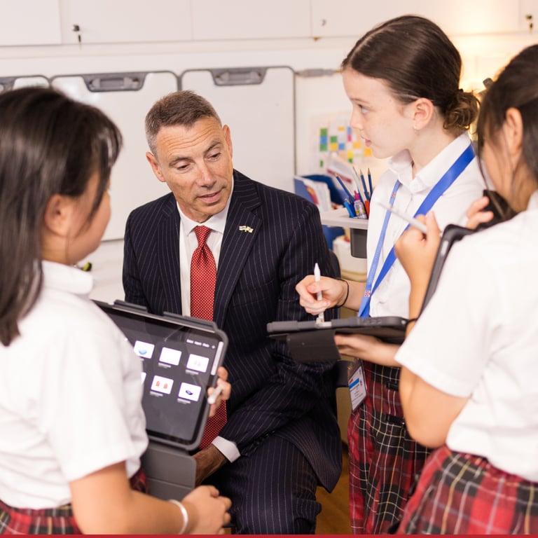 Principal engages with Junior School students using digital tablets, supporting inquiry-based and technology-enhanced learning.