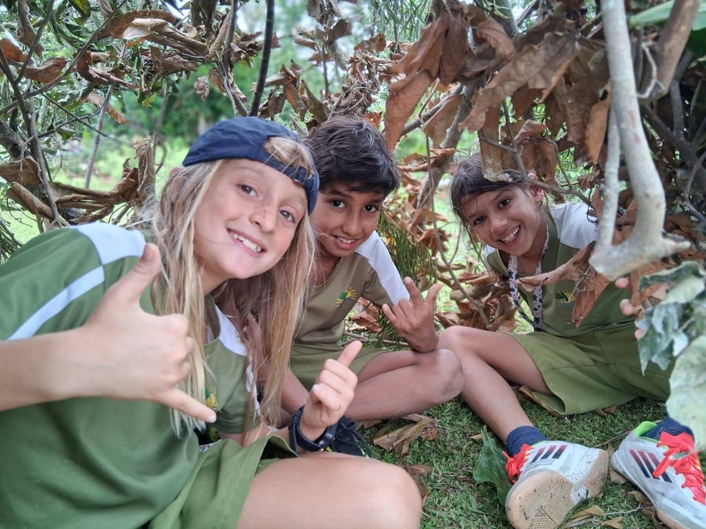 Students smiling while sitting inside a shelter made of branches during an outdoor activity.