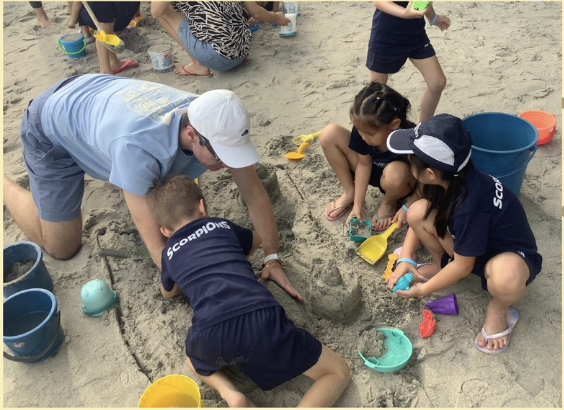 Teacher and students build together in the sand during a beach outing.