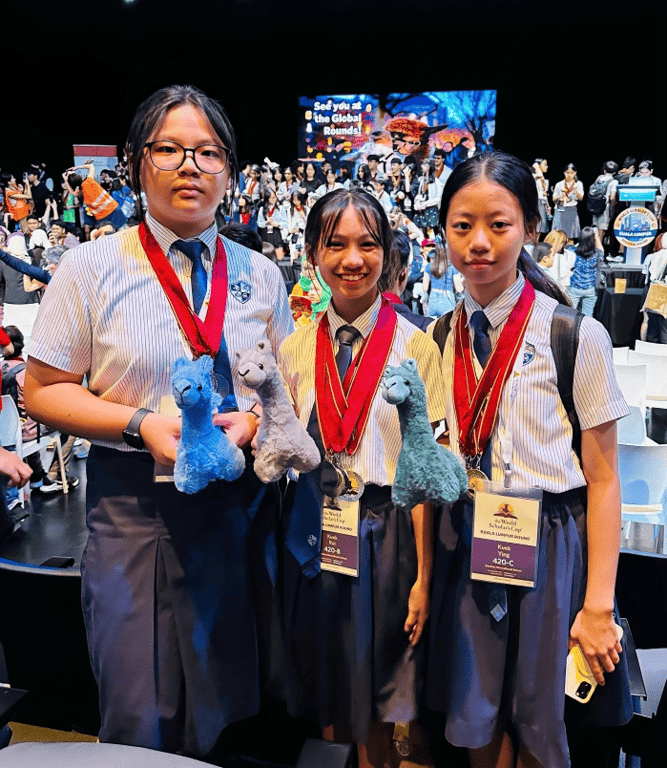 Three proud students pose with medals and mascots after representing the school at an international academic competition.