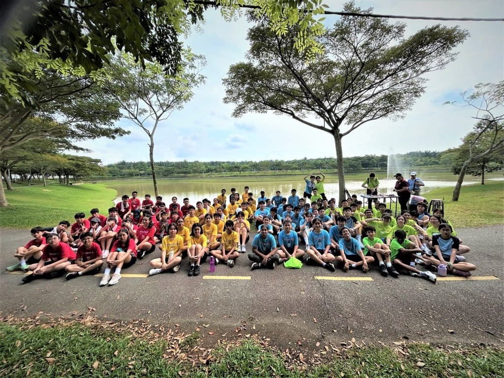 Students from different school houses gather by the lake during a sports or community bonding event.