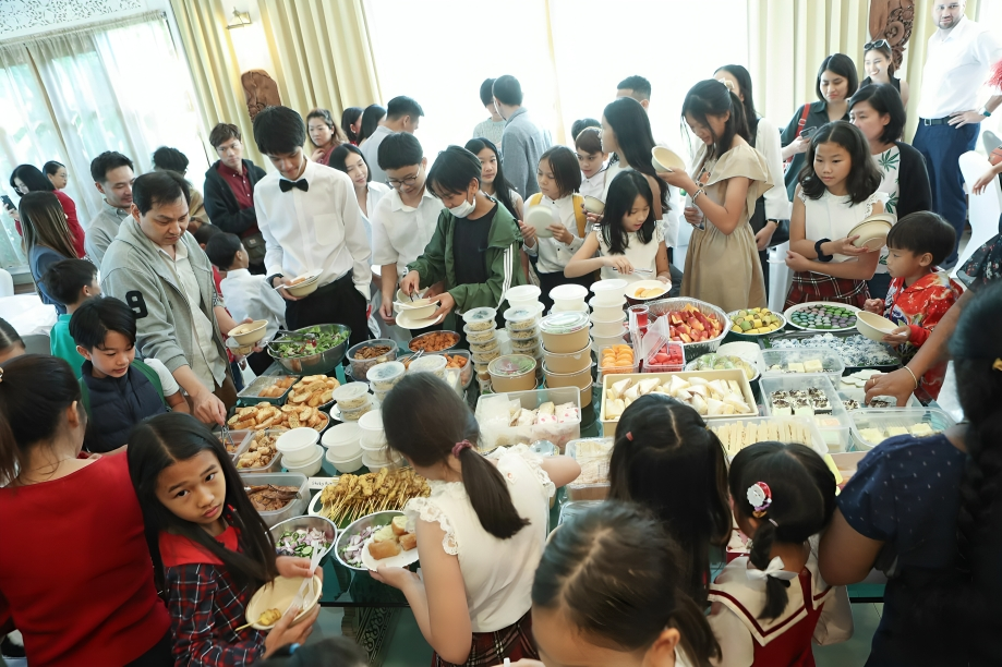 Families and students gather around a feast of homemade dishes, sharing culture and community.