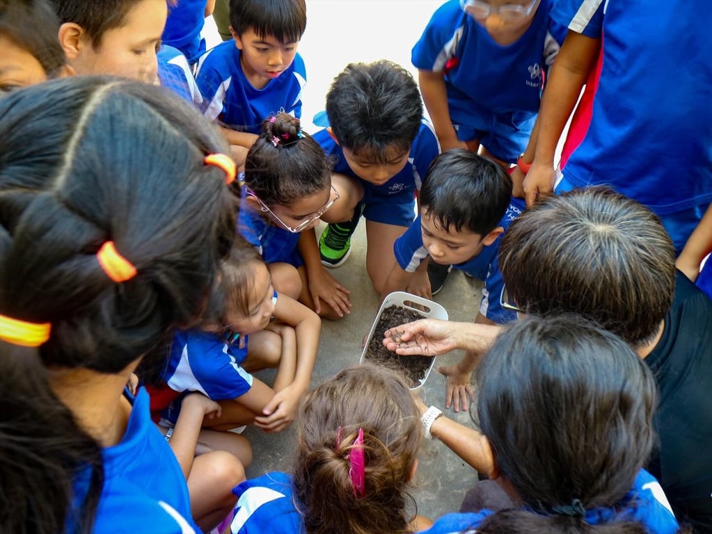 Students gathered around observing worms in soil during a composting activity outdoors.
